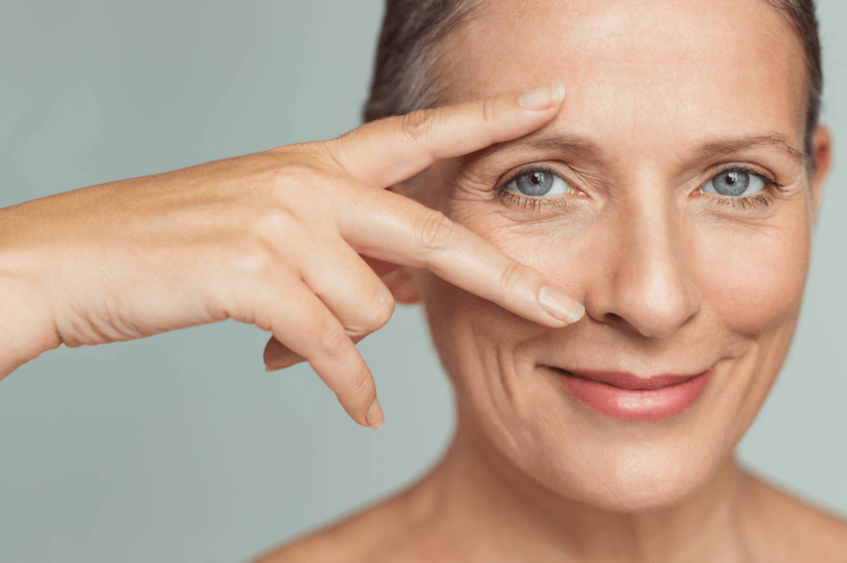 A woman pointing to her eye, emphasizing the area around her eye, likely highlighting a skincare or cosmetic procedure.