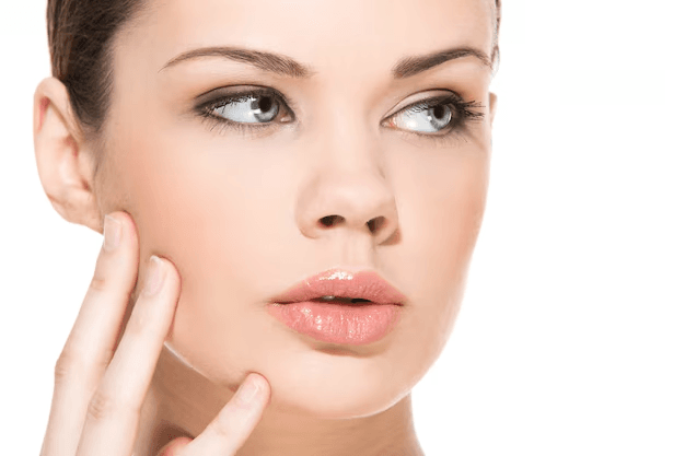 A woman with makeup and styled hair, touching her face with her hand, looking intently to the side.