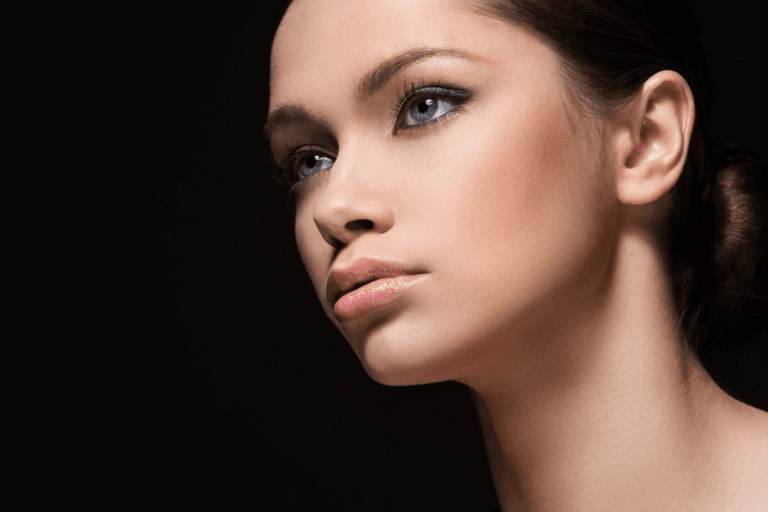 A close-up portrait of a woman with striking blue eyes and dark hair, posed against a black background.
