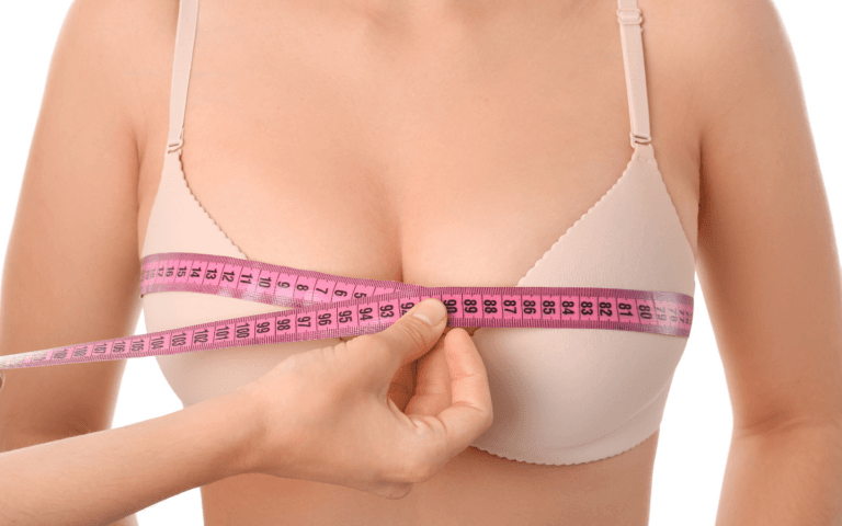 A person measuring their bust size with a tape measure while wearing a light pink bra.
