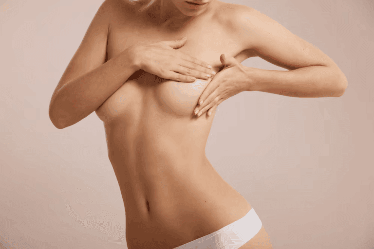 A woman wearing white underwear, covering her breasts with her hands, posing against a light pink background.