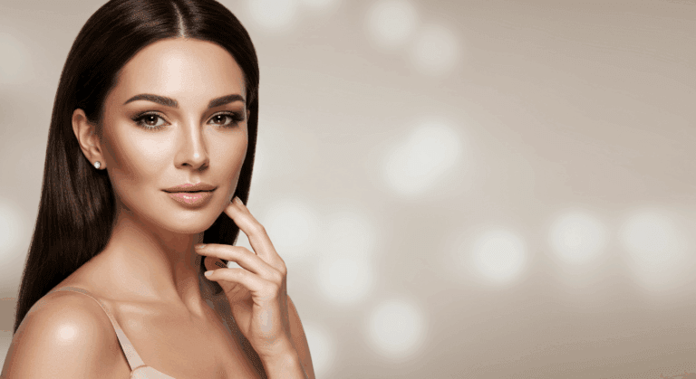 A woman with long, straight dark hair poses confidently with her hand gently touching her face. She has a soft, neutral background with blurred light spots, highlighting her facial features and elegant appearance.