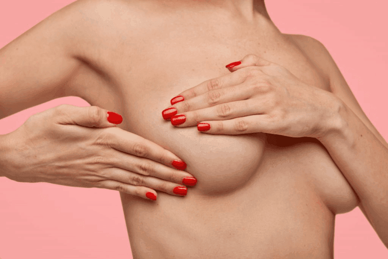 A woman with red nail polish performing a breast self-examination against a pink background.